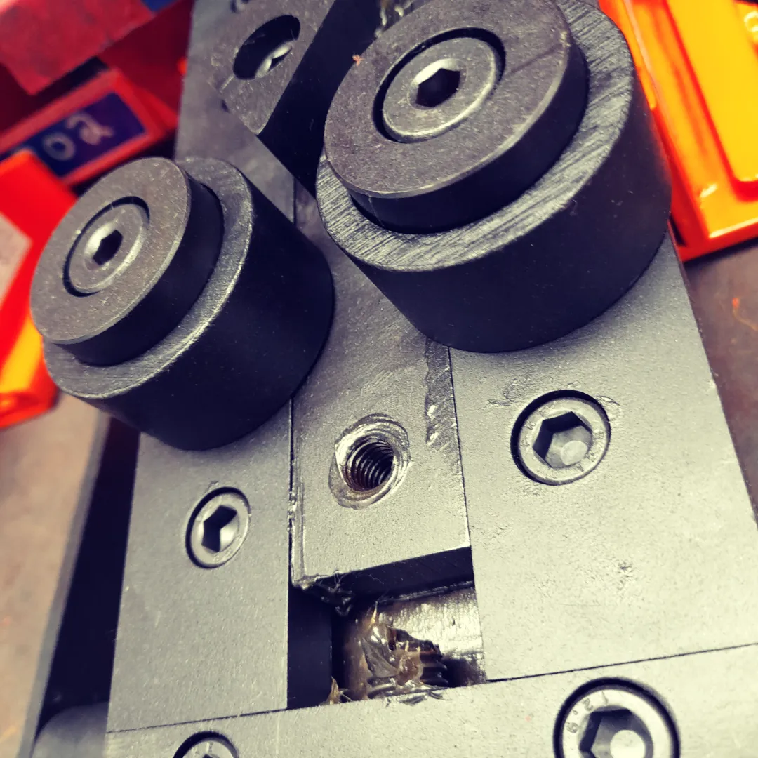 Close-up of blackodised steel rollers and machined metal block with hex bolt fixings on an engineering workbench